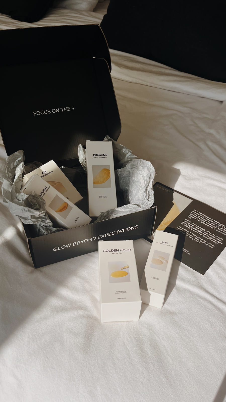 Skincare product from ADDITION SKIN gift box open on a bed, showing Pregame Jelly Cleanser and other products