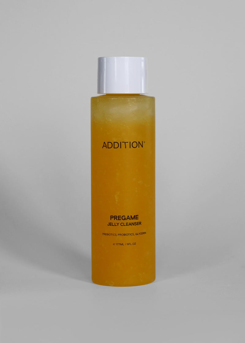 A tall, cylindrical bottle of ADDITION Pregame Jelly Cleanser filled with a translucent golden-yellow liquid, featuring a white cap, set against a solid light gray background.